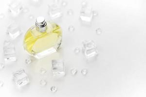 bouteille jaune de parfum féminin, photographie objective de la bouteille de parfum dans des glaçons et de l'eau sur un tableau blanc. vue d'en-haut. photo de produit maquette, concept de fraîcheur