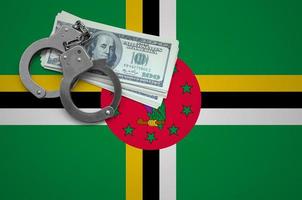drapeau de la dominique avec des menottes et un paquet de dollars. le concept d'enfreindre la loi et les crimes de voleurs photo