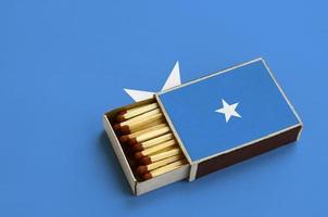 le drapeau de la somalie est affiché dans une boîte d'allumettes ouverte, qui est remplie d'allumettes et repose sur un grand drapeau photo