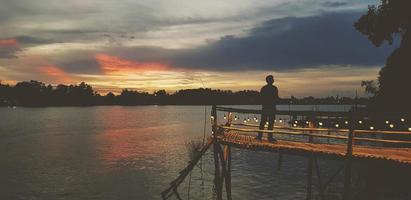 bangkok, thaïlande-29 juin 2022 silhouette d'homme debout sur le bord de l'eau en bois, le front de mer ou le pont avec fond de rive et d'arbre au coucher du soleil ou au soleil. belle nature et liberté. papier peint naturel. photo