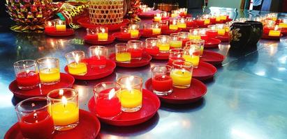 de nombreux verres aux chandelles dans un plateau rouge pour le respect saint sur une table en acier inoxydable au temple chinois ou thaïlandais. religion, croyance des gens. photo