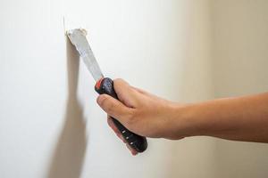 homme réparant un mur blanc fissuré avec une spatule photo