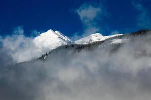 Montagne enneigée s'élevant au-dessus des nuages avec ciel bleu