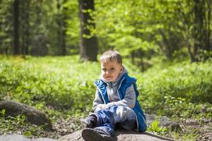 portrait d'un garçon dans un débardeur bleu dans les bois au printemps. promenez-vous dans le parc verdoyant à l'air frais. la lumière magique des rayons du soleil tombe derrière le garçon. photo