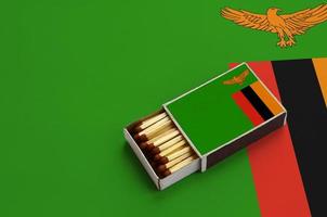 le drapeau de la zambie est affiché dans une boîte d'allumettes ouverte, qui est remplie d'allumettes et repose sur un grand drapeau photo