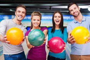 couleurs vives du meilleur jeu. amis joyeux regardant la caméra et étirant leurs balles tout en se tenant contre les pistes de bowling photo