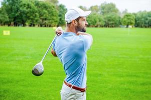 bonne grève. vue latérale d'un golfeur confiant balançant son chauffeur et regardant ailleurs tout en se tenant sur le terrain de golf photo