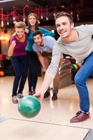 il est prêt à gagner. beaux jeunes hommes lançant une boule de bowling tandis que trois personnes applaudissent photo