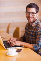avoir la possibilité de travailler partout. beau jeune homme travaillant sur un ordinateur portable et souriant assis dans un café photo