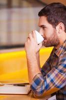 en attente d'inspiration. vue latérale d'un beau jeune homme buvant du café assis dans un café photo