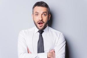 incroyable nouvelles portrait d'un homme mûr surpris en chemise et cravate en gardant la bouche ouverte et en regardant la caméra en se tenant debout sur fond gris photo