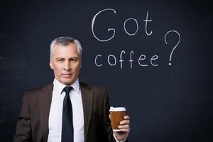 a obtenu du café un homme senior confiant en tenues de soirée tenant une tasse de café et regardant la caméra en se tenant debout contre le tableau noir avec un dessin à la craie dessus photo