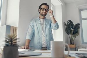 beau jeune homme regardant la caméra et souriant tout en se tenant près de son lieu de travail au bureau photo