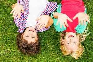 nous aimons la vue de dessus d'été de deux mignons petits enfants levant les mains et souriant tout en étant allongés sur l'herbe verte ensemble photo