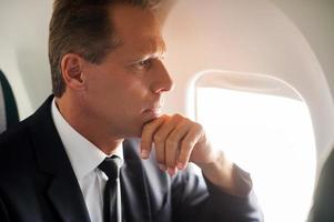 réfléchir à des solutions. homme d'affaires mature réfléchi assis à son siège dans l'avion et regardant à travers la fenêtre de l'avion photo