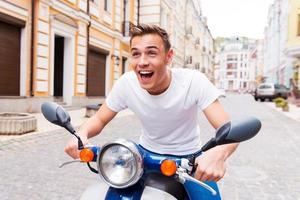 tester son nouveau scooter. heureux jeune homme faisant du scooter le long de la rue et gardant la bouche ouverte photo