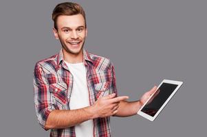 votre publicité peut être ici joyeux jeune homme tenant une tablette numérique et la pointant en se tenant debout sur fond gris photo