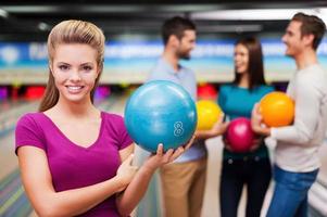 joueur beau et confiant. belles jeunes femmes tenant une boule de bowling tandis que trois personnes communiquant contre les pistes de bowling photo