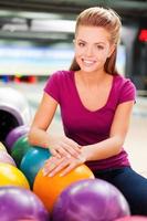 charmant joueur. jeunes femmes gaies se tenant la main sur une boule de bowling et souriantes assises contre des pistes de bowling photo