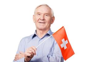 homme senior avec drapeau suisse. joyeux homme âgé tenant le drapeau de la suisse et souriant à la caméra en se tenant debout sur fond blanc photo