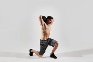 jeune homme confiant avec un corps parfait faisant de l'exercice avec un ballon de médecine sur fond blanc photo