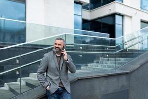 un homme d'affaires adulte vêtu d'une veste d'automne parle sur un téléphone portable dans le contexte d'un escalier menant à un centre d'affaires, à un concept d'assurance entreprise et risque photo