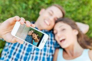 capturer les émotions lumineuses. vue de dessus d'un jeune couple d'amoureux heureux faisant du selfie avec un téléphone intelligent en position allongée sur l'herbe. photo