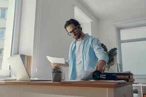 jeune homme confiant faisant de la paperasse tout en se tenant près de son lieu de travail au bureau photo