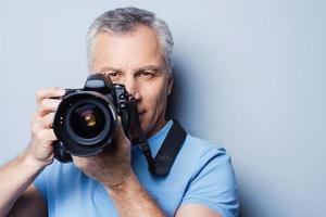 sourire portrait d'un homme senior confiant en t-shirt tenant la caméra en se tenant debout sur fond gris photo