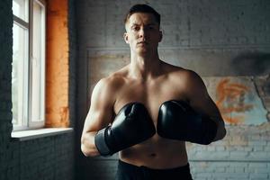 jeune homme confiant dans des gants de boxe regardant la caméra tout en se tenant dans la salle de gym photo