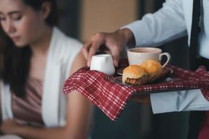 serveur tenant des assiettes avec du pain et une tasse de café tout en servant des invités dans un restaurant. photo