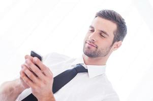taper un message d'affaires. vue en angle bas d'un beau jeune homme en chemise et cravate tapant un message sur le téléphone portable et souriant photo