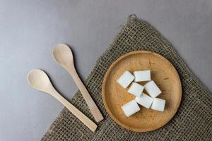 cubes de sucre dans une assiette en bois avec des cuillères sur un sac sur la table de la cuisine. vue de dessus. photo