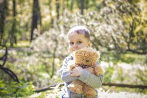 un garçon mignon joue avec un ourson dans la forêt. les rayons du soleil enveloppent l'espace de la clairière d'une souche. une histoire magique d'interactions pour le livre. espace pour la copie. sélectif photo