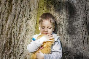 un garçon mignon joue avec un ourson dans la forêt. les rayons du soleil enveloppent l'espace. une histoire magique d'interactions pour le livre. espace pour la copie. photo