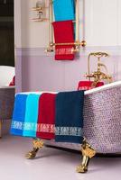 une photo verticale de serviettes en bambou colorées accrochées à une baignoire violette en mosaïque dans une salle de bains