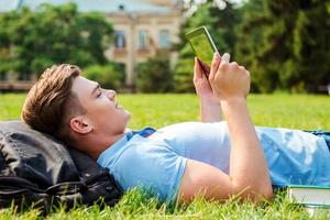 trouver un endroit paisible pour se détendre. vue latérale d'un beau jeune homme travaillant sur une tablette numérique en position couchée sur l'herbe photo