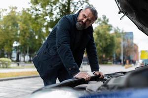 un homme essaie de comprendre la panne de la voiture debout devant le capot ouvert, concept d'assurance automobile photo