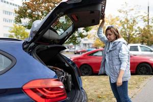 une jeune femme mère a chargé une poussette dans la voiture et se tient près du coffre de la voiture photo