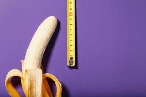 concept de pénis de banane jaune mesuré par un ruban à mesurer sur fond violet. photo