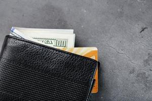 un portefeuille noir avec des billets de banque et une carte électronique dorée sur fond de pierre gris foncé. photo