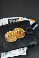 un portefeuille noir avec des dollars, des cartes électroniques et des bitcoins sur un fond texturé noir. photo