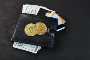 un portefeuille noir avec des dollars, des cartes électroniques et des bitcoins sur un fond texturé noir. photo