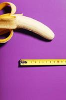 concept de pénis de banane jaune mesuré par un ruban à mesurer sur fond rose. comparaison de la taille de la dignité d'un homme. photo