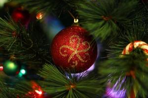 boule de noël rouge brillante sur un sapin avec des décorations de noël et des lumières floues. photo