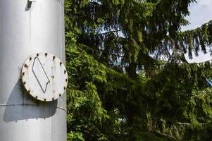 grande colonne de réservoir industriel en acier inoxydable brillant en fer avec une trappe ronde pliante, trou d'homme avec boulons, écrous et goujons sur fond d'arbres verts et de bois photo