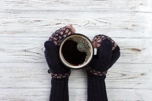 mains féminines dans des mitaines tenant une tasse de café sur fond de bois photo