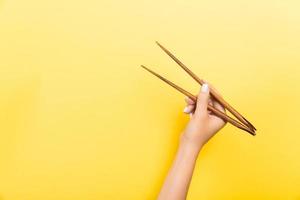 main féminine avec des baguettes sur fond jaune. cuisine asiatique traditionnelle avec espace vide pour votre conception photo