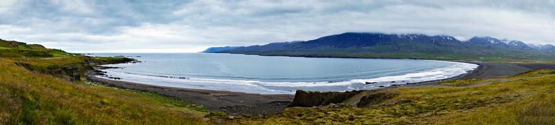 vue panoramique sur la baie de l'atlantique nord sur fond de montagnes et de ciel nuageux. paysage d'automne d'islande avec de l'herbe verte jaune photo