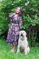 belle jeune femme marche avec son chien de berger russe du sud dans un parc d'été avec des buissons de lilas en fleurs. photo